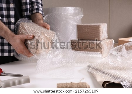 Man covering box with bubble wrap at table in warehouse, closeup Royalty-Free Stock Photo #2157265109