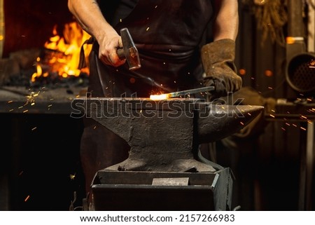 Ancient professions in the modern world. Bearded man, blacksmith manually forging the molten metal on the anvil in smithy with spark fireworks. Concept of labor, retro vintage occupation, family Royalty-Free Stock Photo #2157266983