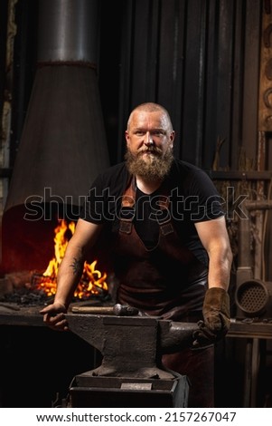 Ancient professions in the modern world. Bearded man, blacksmith manually forging the molten metal on the anvil in smithy with spark fireworks. Concept of labor, retro vintage occupation, family Royalty-Free Stock Photo #2157267047