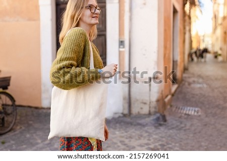 Young Girl holding white cotton tote bag on old town background. Mockup and zero waste concept. Eco Nature Friendly Style. Environmental Conservation Recycling mock up