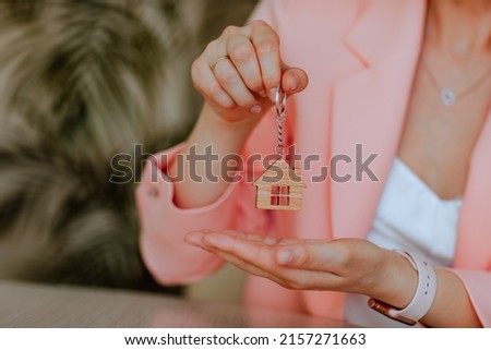 Woman holds small wooden keychain like a house in hands. Development and rent concept. Focus is at the house Royalty-Free Stock Photo #2157271663