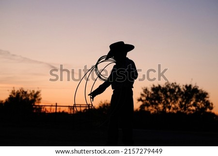 Young cowboy with rope in Texas sunset on ranch for childhood western lifestyle. Royalty-Free Stock Photo #2157279449