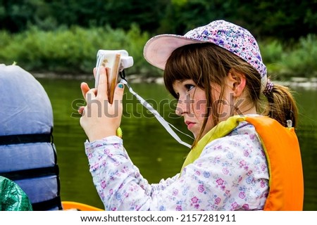 close-up of a girl in an orange life jacket takes pictures of nature in a boat on the river with a smartphone