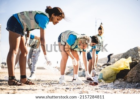 Diverse people cleaning up the beach, volunteers collecting the waste on the coast line, young people working in team aware of the pollution produced by the plastic industry Royalty-Free Stock Photo #2157284811