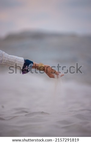 A vertical shot of a woman with sand falling through her hands near the beach at sunset
