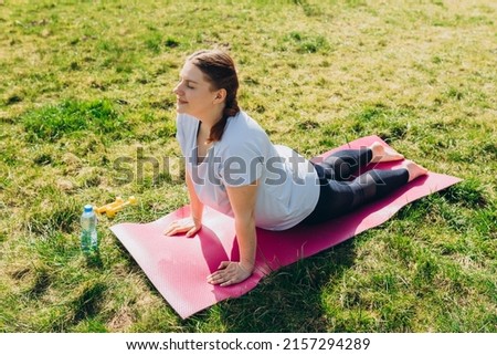 Girl practicing cobra pose, full length. Portrait of young woman practicing yoga on nature background. Relaxing and doing yoga. Wellness and healthy lifestyle. Bhujangasana
