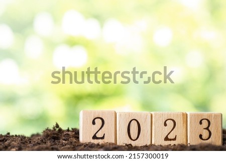 Wooden blocks lie on a wooden table against the backdrop of a summer garden and create the word 2023. New Year Concept