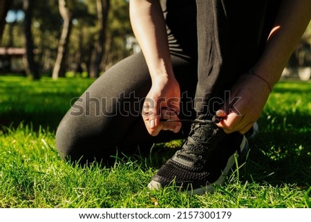 Cropped view of millennial woman tying her shoelaces on grass at city park, outdoors. Fitness woman tying shoelaces before training.