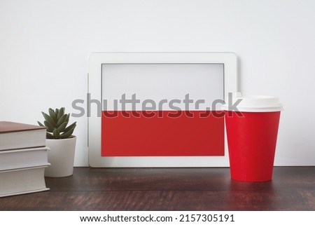 National flag of Poland on the tablet, textbooks, a red cup of hot drink coffee or tea on the table, the concept of learning polish Royalty-Free Stock Photo #2157305191
