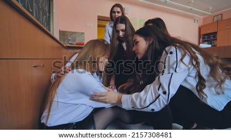 Pupils run to calm down their friend who is crying on the floor in the classroom. Royalty-Free Stock Photo #2157308481
