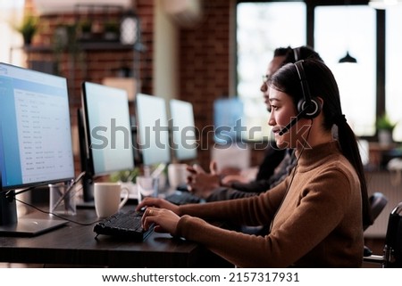 Paralyzed asian employee working at call center reception in disability friendly office. Female operator wheelchair user with impairment giving assistance on customer service helpline. Royalty-Free Stock Photo #2157317931