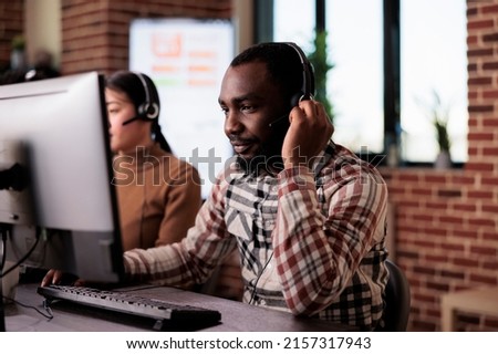 African american call center operator talking to clients on helpline, giving telemarketing assistance to people at customer care service. Helpdesk support consultant working at network reception. Royalty-Free Stock Photo #2157317943