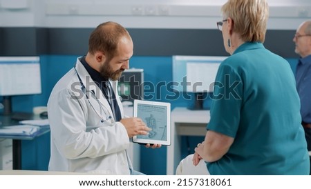 Male doctor showing human skeleton illustration on digital tablet to senior woman at checkup examination. Physician and patient looking at osteopathy diagnosis with bones and spinal cord. Royalty-Free Stock Photo #2157318061