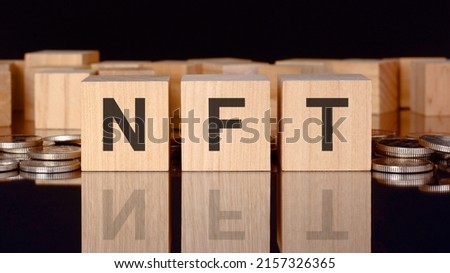 NFT - short for Non Fungible Token. text on wood cubes with coins, black background, business concept. the inscription on the cubes is reflected from the surface of the black table. front view