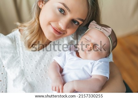 Young beautiful mother with blue eyes holds her little newborn daughter in her arms. Motherhood. Care. Baby. Home.
