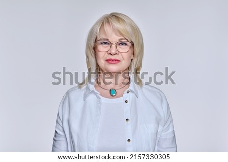 Portrait of mature woman in glasses looking at camera on light background