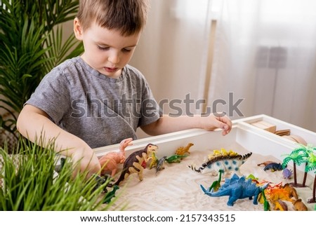 Cute baby boy playing sensory box dinosaur world kinetic sand table with carnivorous and herbivorous dinosaurs. Male kid enjoying early development game fine motor skills with Montessori material Royalty-Free Stock Photo #2157343515