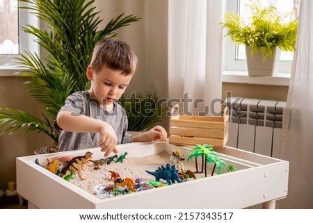 Cute baby boy playing sensory box dinosaur world kinetic sand table with carnivorous and herbivorous dinosaurs. Male kid enjoying early development game fine motor skills with Montessori material Royalty-Free Stock Photo #2157343517