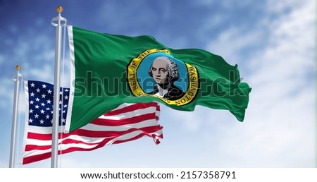 The Washington state flag waving along with the national flag of the United States of America. Washington is a state in the Pacific Northwest region of the Western United States