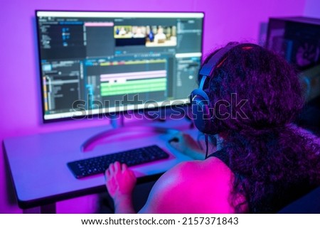 Person using a computer to create content from home. video editor, pc gamer. Young Latin American using the computer at night, editing videos and exporting audiovisual pieces. 