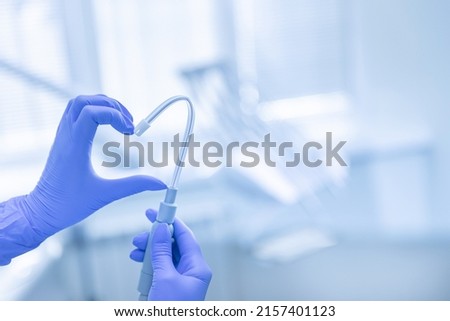 Hand in blue latex glove with saliva ejector symbolize love heart dental background. Royalty-Free Stock Photo #2157401123