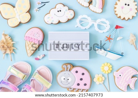 July text on lightbox and cute summer symbols on blue background. Top view, Flat lay. Creative summer concept, greeting card.