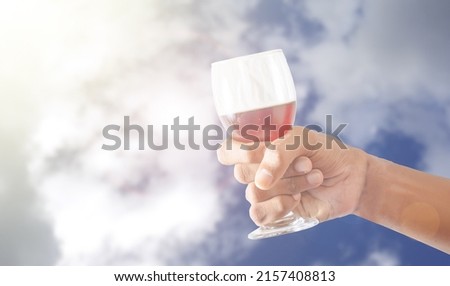 a photo of man holding glass with wine on blue sky background
