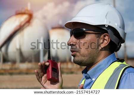 Person in helmet using radio communication and point hand tojob. person in helmet with oil tanks in the desert onbackground.