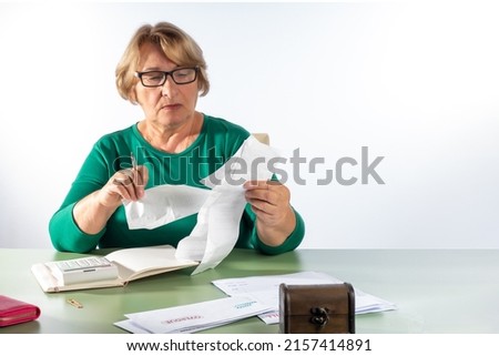 A pensioner woman checks shop receipts. The concept of accounting for household expenses, rising cost of living, rising energy prices, retirement savings, investments.