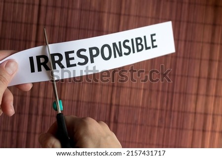 human hand cuts with scissors a piece of paper with the inscription irresponsible Royalty-Free Stock Photo #2157431717