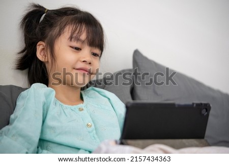 Girl lying in bed watching cartoons on tablet at home.