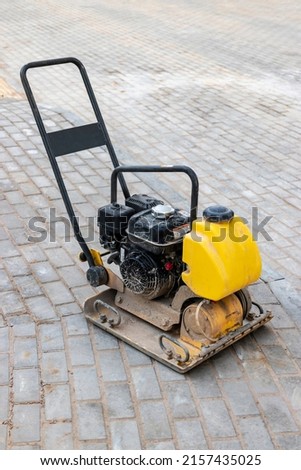 Vibratory rammer with vibrating plate on a construction site. Compaction of the soil before laying paving slabs. Close-up Royalty-Free Stock Photo #2157435025