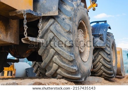 Big rubber wheels of soil grade tractor car earthmoving at road construction side. Close-up of a dirty loader wheel with a large tread against the sky Royalty-Free Stock Photo #2157435143
