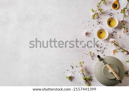 Green Tea and Cherry Blossom on white background, top view, copy space. Traditional Japanese cast iron teapot and cups, asian green tea composition with spring sakura bloom.