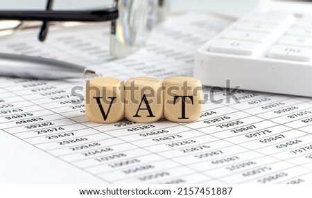 wooden cubes with the word VAT stand on financial background with chart, calculator, pen and glasses, business concept.