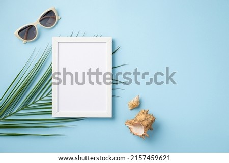 Summer vacation concept. Top view photo of white photo frame sunglasses shells and palm leaves on isolated pastel blue background with empty space