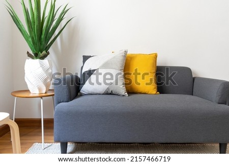 White and yellow pillows on a grey sofa with coffee table in Scandinavian living room interior.
