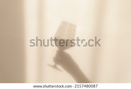 Abstract silhouette shadows hand holding glass of wine in the rays the sun reflected on wall. Blurry and out of focus. Royalty-Free Stock Photo #2157480087