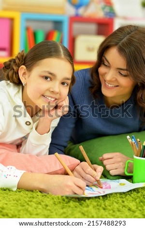 little cute girl with mother drawing lying on the floor at home