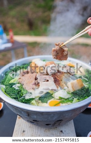 closeup hand holding chopsticks picking up grilled pork from pan, thai style pork barbecue Royalty-Free Stock Photo #2157495815