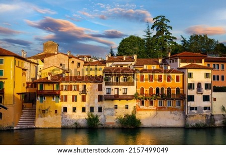 Bassano del Grappa, Veneto, Italy. Ancient italian houses on river Brenta. Panoramic view at old town with vintage buildings of Alpine mountains scenic sunset landscape. Royalty-Free Stock Photo #2157499049