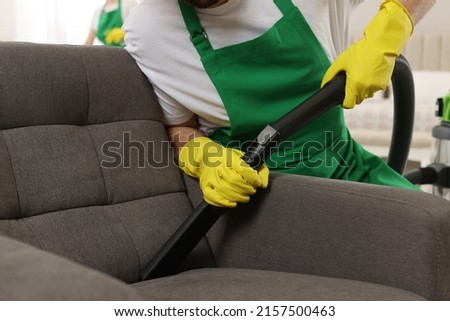 Professional janitor vacuuming armchair in room, closeup Royalty-Free Stock Photo #2157500463