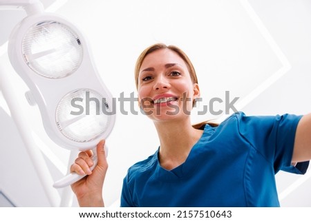 Low angle view of female dentist adjusting reflector lights above patient's head sitting in dental chair Royalty-Free Stock Photo #2157510643