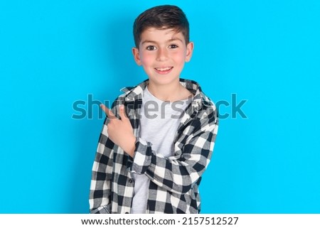 caucasian kid boy wearing plaid shirt over blue background pointing away and smiling to you. Look over there! Royalty-Free Stock Photo #2157512527