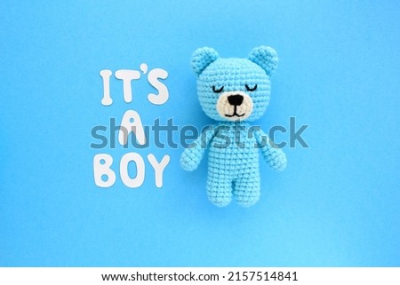 It's a boy letters, crochet plush soft bear on blue background. Baby boy birth, new life, family concept. Gender reveal party. Greeting card idea for newborn. Pregnancy announcement. Flatlay, top view