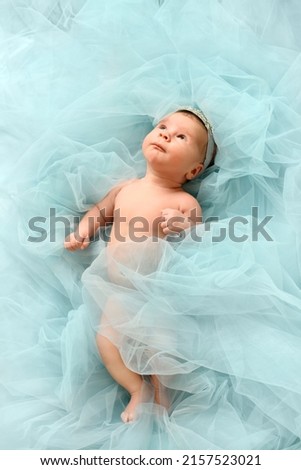 Infant baby princes with crown lye in cloud of pastel blue background and look up