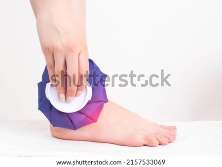 The girl applies a medical ice bag to the ankle joint to eliminate pain and relieve swelling. Cold joint treatment, inflammation Royalty-Free Stock Photo #2157533069