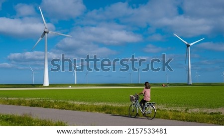 young woman electric green bike bicycle by windmill farm, windmills isolated on a beautiful bright day Netherlands Flevoland Noordoostpolder Royalty-Free Stock Photo #2157533481