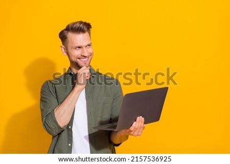 Portrait of attractive minded cheerful guy hacker geek using laptop deciding order booking isolated over bright yellow color background