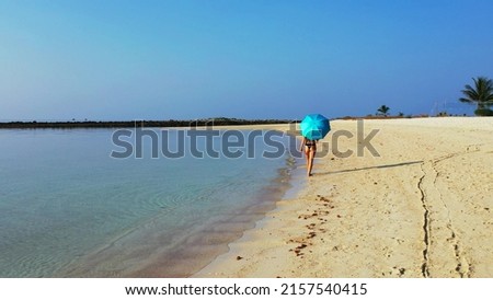 A woman under an umbrella walking on the sand in Koh Samui, Thailand, Asia